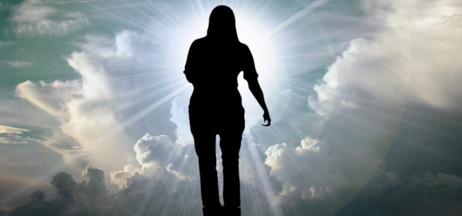 Silhouette of a person walking through clouds toward a bright light.