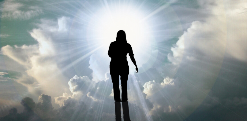 Silhouette of a person walking through clouds toward a bright light.